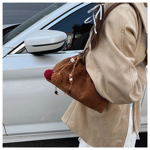 Détail du sac seau en daim marron avec pompons colorés et perles en bois sur la bandoulière