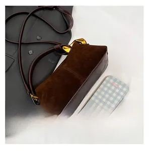 Detail of a dark brown suede crossbody bag with gold chain buckle next to a smartphone