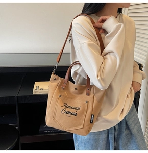 Detail of canvas tote bag showing front utility pocket and leather carry handles