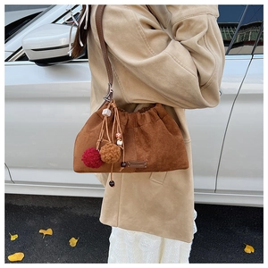 Détail du sac seau en daim marron avec pompons décoratifs et logo en cuir PANTORE
