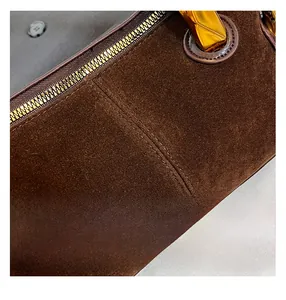 Macro detail of brown suede handbag featuring golden zipper and precision double stitching