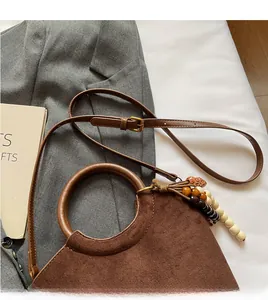 Detail of dark brown suede bucket bag featuring a round ring handle and beaded tassel
