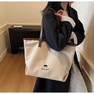 Detail of canvas tote bag featuring embroidered cartoon girl and brown leather trim accents