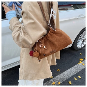Détail d'un sac seau en daim marron avec cordon de serrage et pompons en peluche colorés