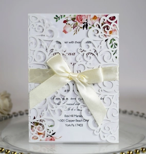 Macro detail of laser-cut lace wedding invitation with elegant ribbon bow and floral insert