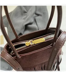Détail de la fermeture éclair dorée et texture en daim marron sur le sac à franges