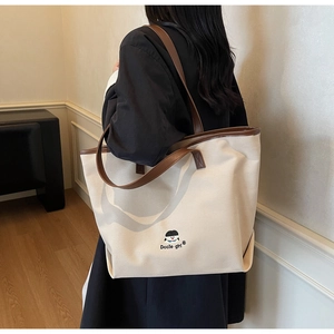 Detail of large canvas tote bag with embroidered boy motif and brown leather handles