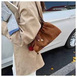Détail du sac seau en daim marron avec pompons en peluche et perles en bois