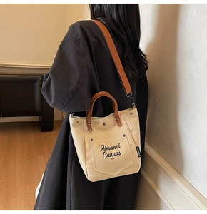 Detail of canvas tote bag showing brown leather handles and adjustable shoulder strap