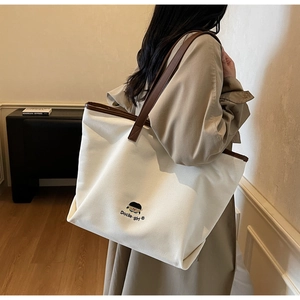 Detail of canvas tote bag with brown leather handles and Docile-girl embroidery