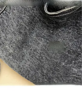 Close-up of washed black denim texture with white contrast stitching detail on tote bag