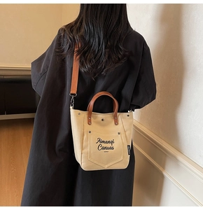 Detail view of canvas tote bag with brown leather handles and orange crossbody strap