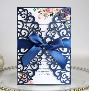 Detail of laser-cut lace wedding invitation with navy sleeve and blue satin ribbon