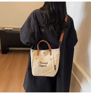 Detail of canvas tote bag with brown leather handles and brand lettering on side