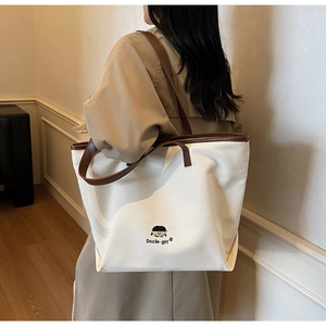 Detailed view of canvas tote bag with brown leather handles and girl embroidery on model