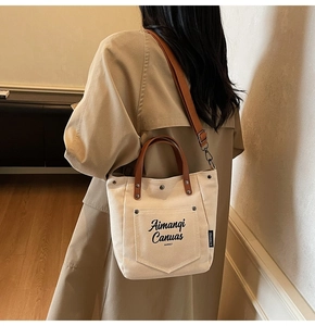 Lifestyle view of cream canvas tote bag with brown straps worn with a trench coat