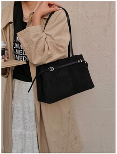Détail d'un sac cabas noir mat avec boucle argentée porté avec un trench-coat kaki