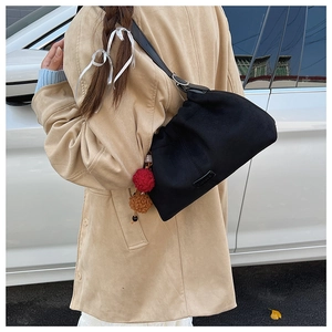 Détail d'un sac hobo plissé noir avec breloques en peluche porté par un mannequin