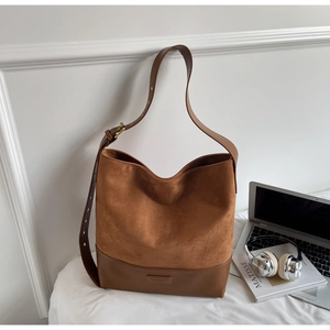 Detail of caramel brown suede tote bag with adjustable leather strap on white bedding
