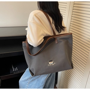 Detail view of large dark grey canvas tote bag with brown leather straps and embroidery