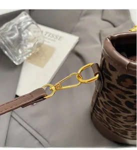Close-up of golden metal hook and brown leather trim on a leopard print barrel handbag