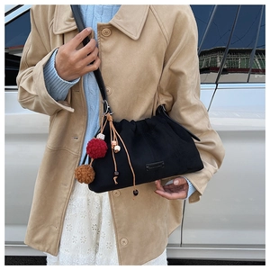 Détail du sac seau noir en daim avec pompon décoratif et breloque en perles