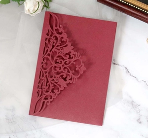Gros plan d'un faire-part bordeaux découpé au laser avec motifs floraux sur marbre blanc