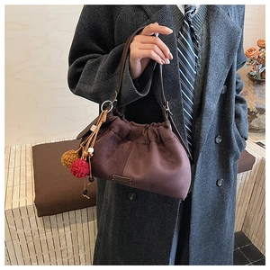 Détail du sac seau plissé en daim marron foncé avec un pendentif pompon décoratif