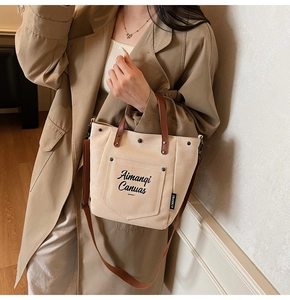 Detail of off-white canvas tote bag with brown leather handles and side brand label
