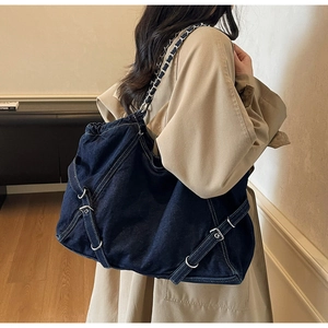 Close-up of dark denim tote with white stitching and silver hardware on a shoulder strap