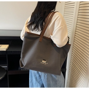 Detail of dark grey canvas tote bag with brown leather handles and character embroidery