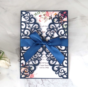 Detail view of laser-cut navy blue lace wedding invitation with ribbon and floral insert