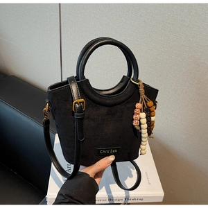 Detail of black suede handbag showing beaded tassel and metallic brand name plate