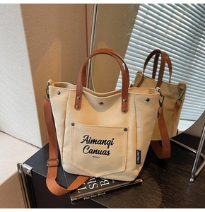 Detail showing the cream canvas tote bag with brown leather handles on a mirror surface