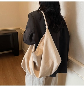 Close-up of beige suede shoulder bag featuring a decorative knot detail on the strap