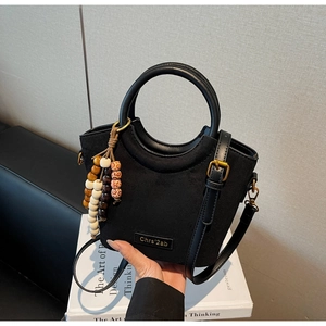 Detail of black bucket bag featuring matte texture, round handle, and colorful wood bead charm