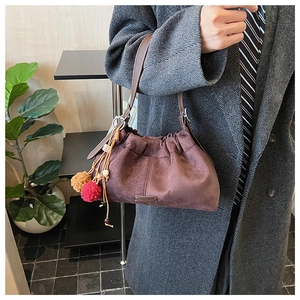 Détail du sac seau en daim marron foncé avec breloques en peluche et bandoulière en cuir