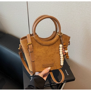 Detail of brown suede bucket bag with leather splicing, curved handle and beaded charm