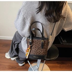 Detail view of leopard print bucket bag with gold logo and beaded charm on grey sweater