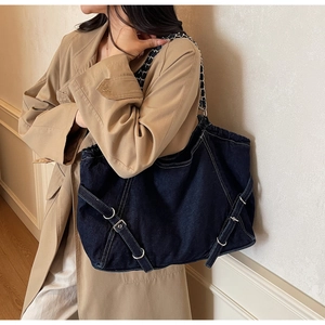 Detail view of the silver metal buckles and cross strap design on dark blue denim bag