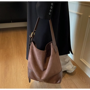 Close-up of brown suede bucket bag featuring adjustable strap and gold hardware accents