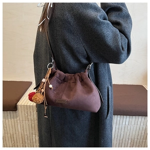 Détail du sac seau en daim marron avec pompons perlés colorés et plaque logo métallique