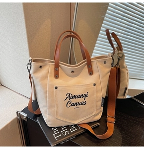 Close-up of canvas tote bag featuring brown leather handles and brand logo detail