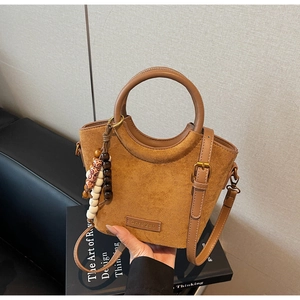 Close-up of brown frosted bucket bag with round handles and colorful ethnic bead charm