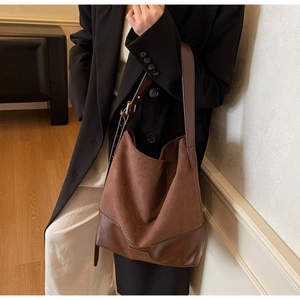Detail of the brown suede tote bag featuring a leather logo patch and stitched bottom