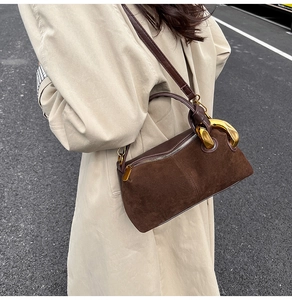 Brown suede crossbody bag with decorative gold buckle on a beige trench coat background
