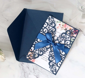 Detail of laser-cut lace wedding invitation with navy blue ribbon and floral design