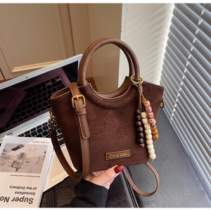 Close-up of brown suede bucket bag with wooden bead charm beside a laptop