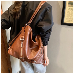 Detail of caramel brown pebble leather texture and silver zipper on motor-style tote bag