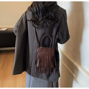 Détail d'un sac bandoulière en daim marron foncé avec de longues franges sur modèle